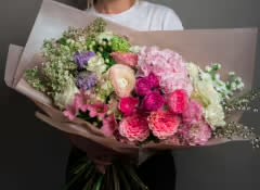 Handheld bouquet of pink, white, and purple flowers wrapped in paper