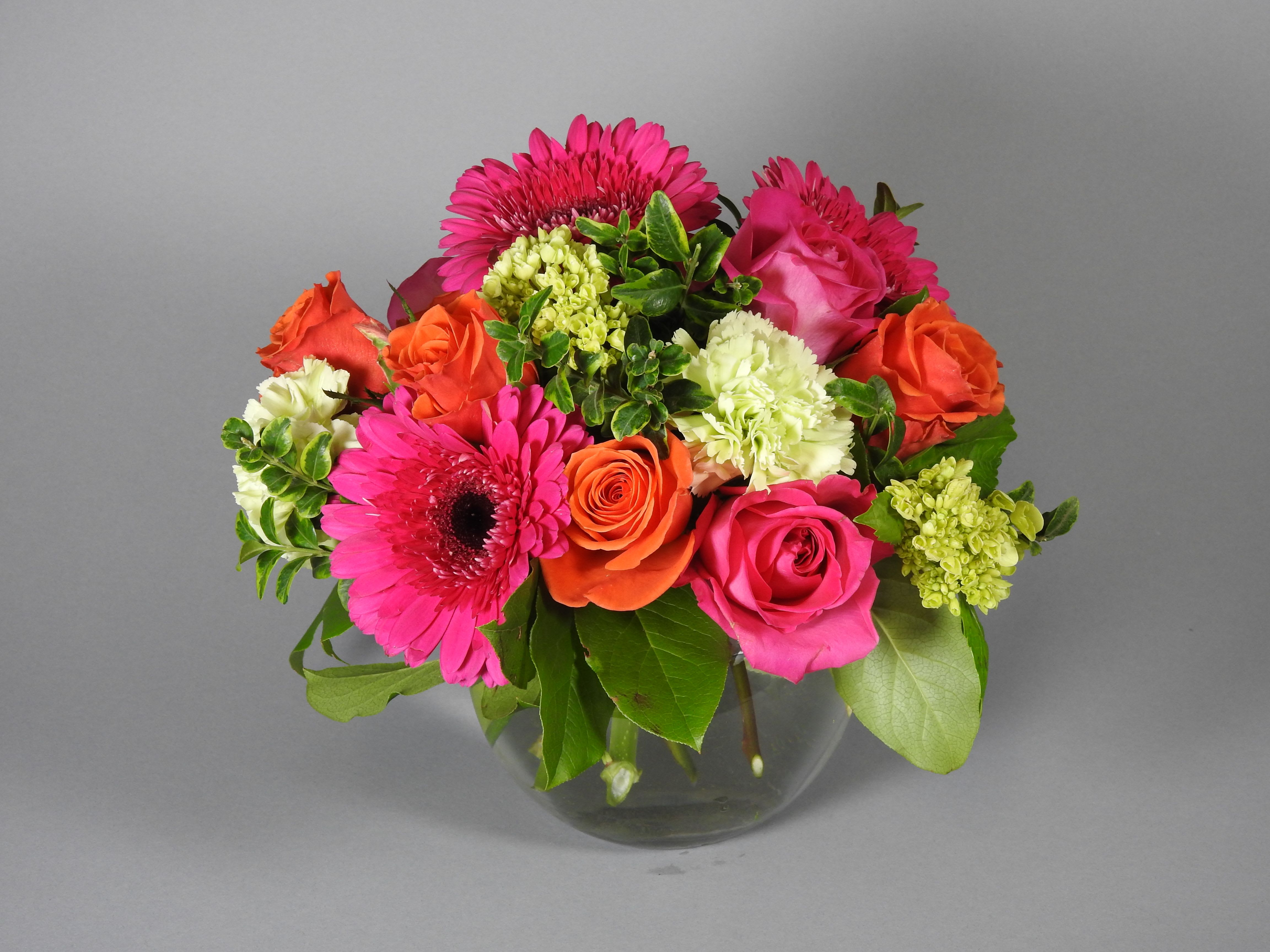 Mixed bouquet of pink gerberas, roses, and orange blooms in a glass vase