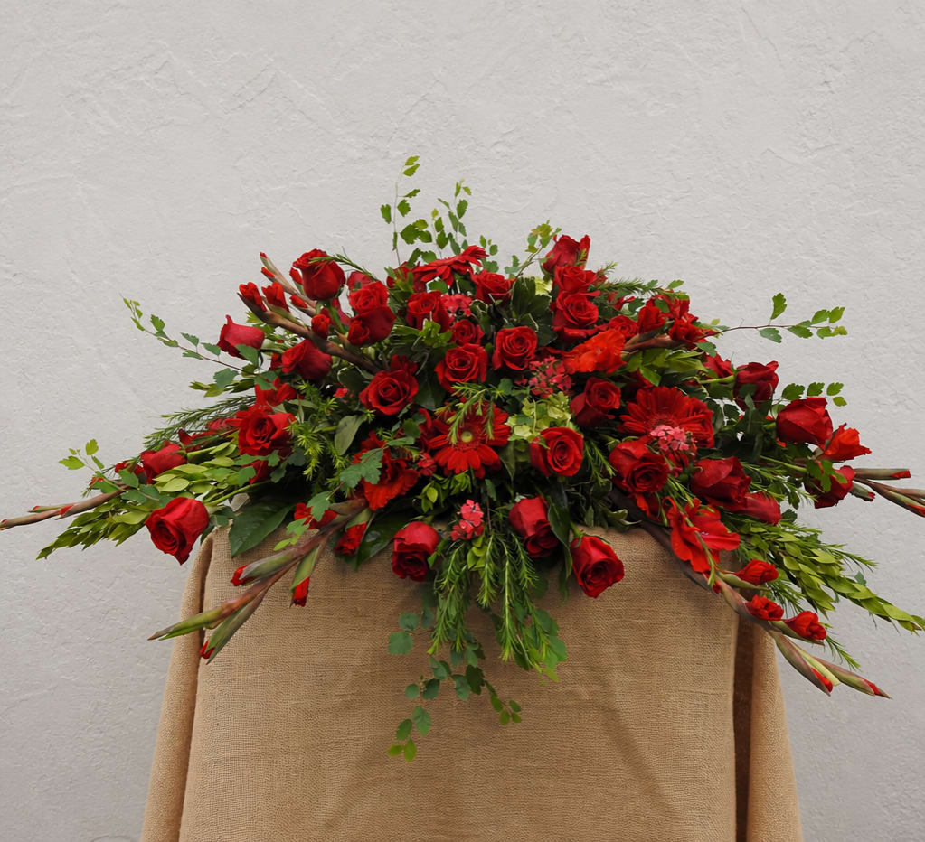 Large red rose arrangement with mixed greenery on a draped stand