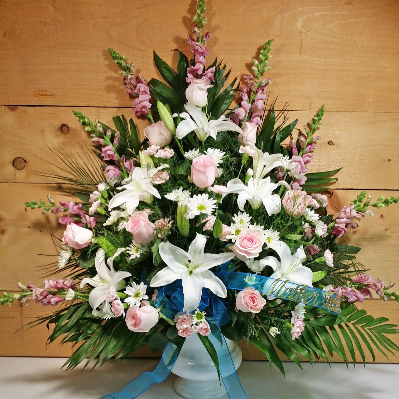 White lilies and pink roses arranged in a white vase with a blue ribbon