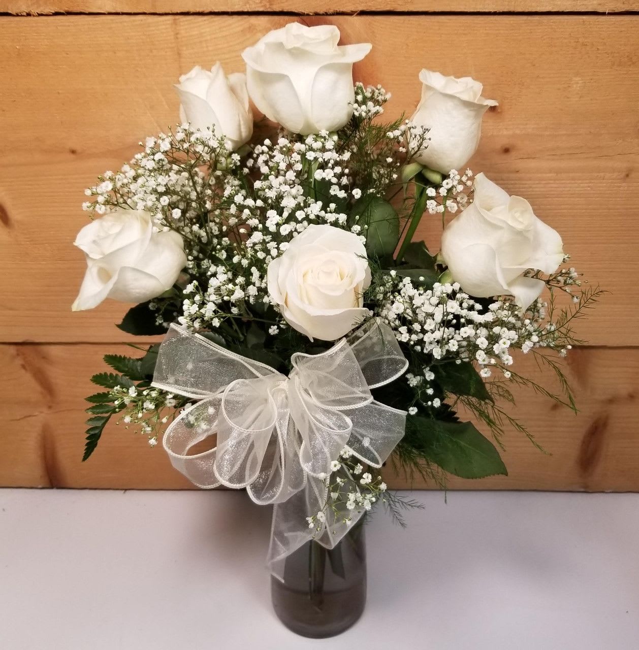 White roses and baby's breath in a glass vase with a sheer bow