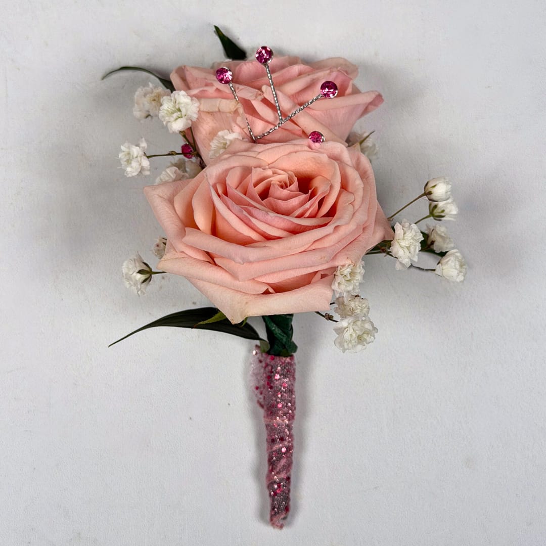Rose Quartz Boutonniere - With Wrap and Sparkle - Two pale blush roses sit snugly together in this Rose Quartz boutonniere, perfectly made for prom night. The soft pink and white palette reads romantic and refined, and the foliage gives depth and contrast to the lighter colored blooms.  This version of this design is the most spectacular of them all, with a shimmering pink sheer ribbon wrap creating a simple but lovely shine to this boutonniere, and a stem of pink rhinestone sparkle accents is the final dazzling touch to make your night even more special. A boutonniere pin is included so it sits neatly on a suit or jacket without any fuss so you can spend your evening dancing the night away.  If you want to change the color of either the ribbon wrap or the sparkle accents, check out our add-ons below or at checkout and pick your desired color.