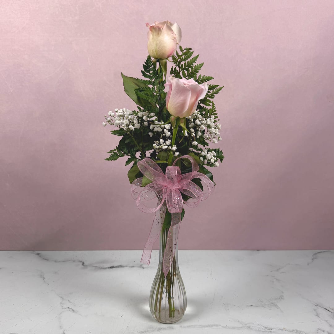 Two pale pink roses in a clear glass vase with a pink ribbon