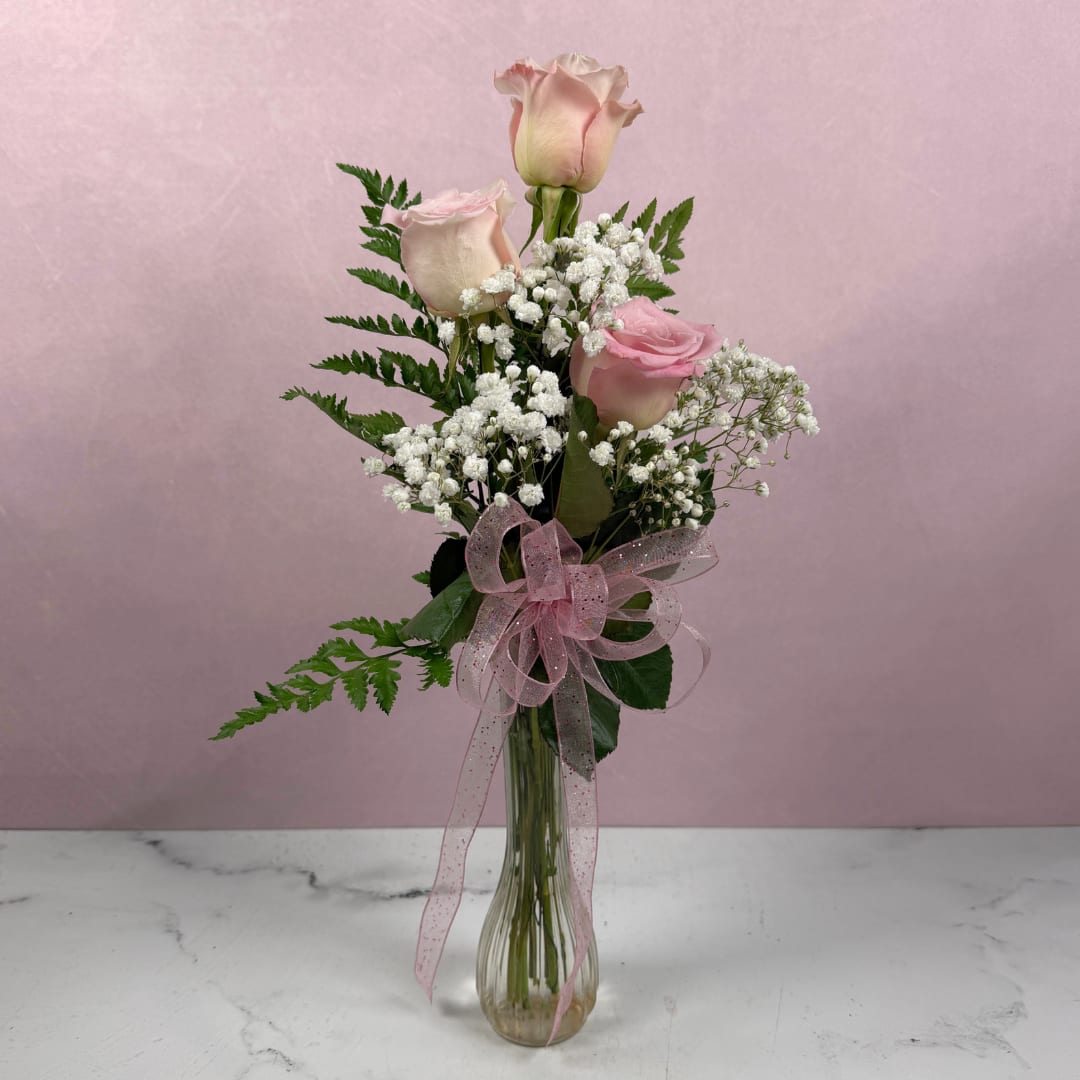 Pink roses with baby's breath in a clear glass vase tied with a pink ribbon.