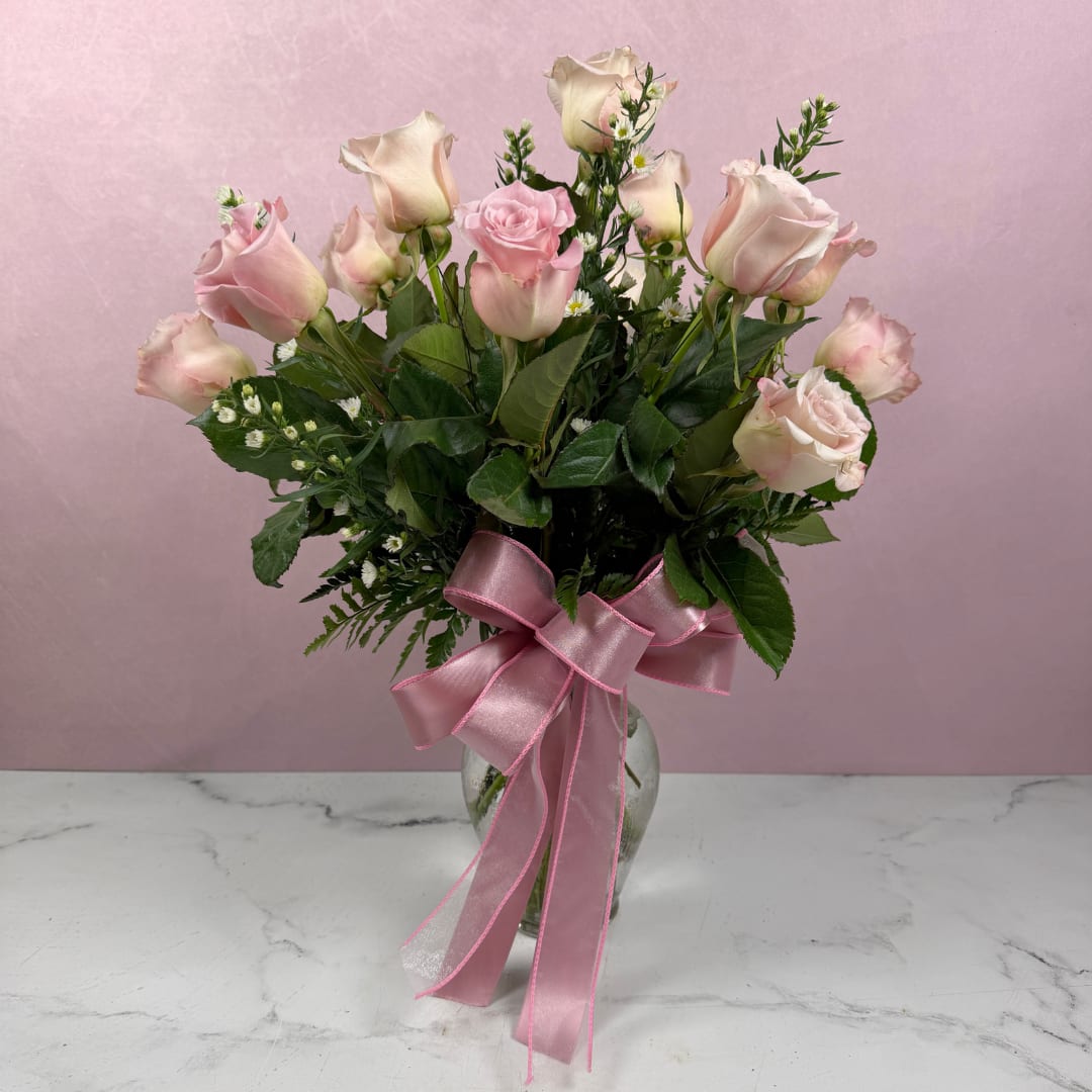 Pink and cream roses in a glass vase with a pink ribbon bow
