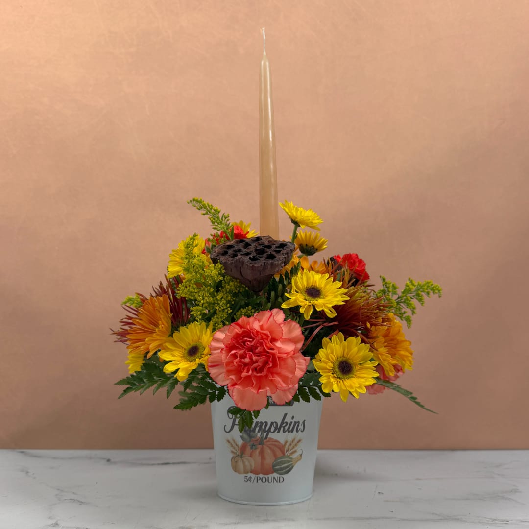 Fall flower arrangement in a pumpkin bucket with a tall candle