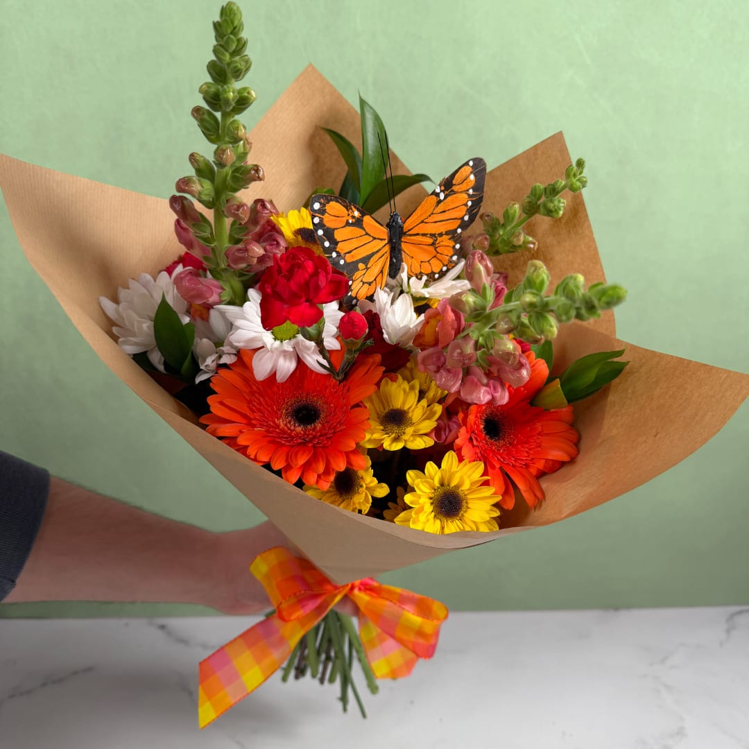 Bright Beauty Butterfly Wrapped Bouquet - The Bright Beauty Butterfly Wrapped Bouquet is a beautiful assortment of warm colored blooms! Orange snapdragons and gerbera daisies are joined with red mini carnations and yellow viking daisies to create a lovely display of flowers, perfect for multiple occasions. No matter what your reason is for giving flowers, these are a great choice!