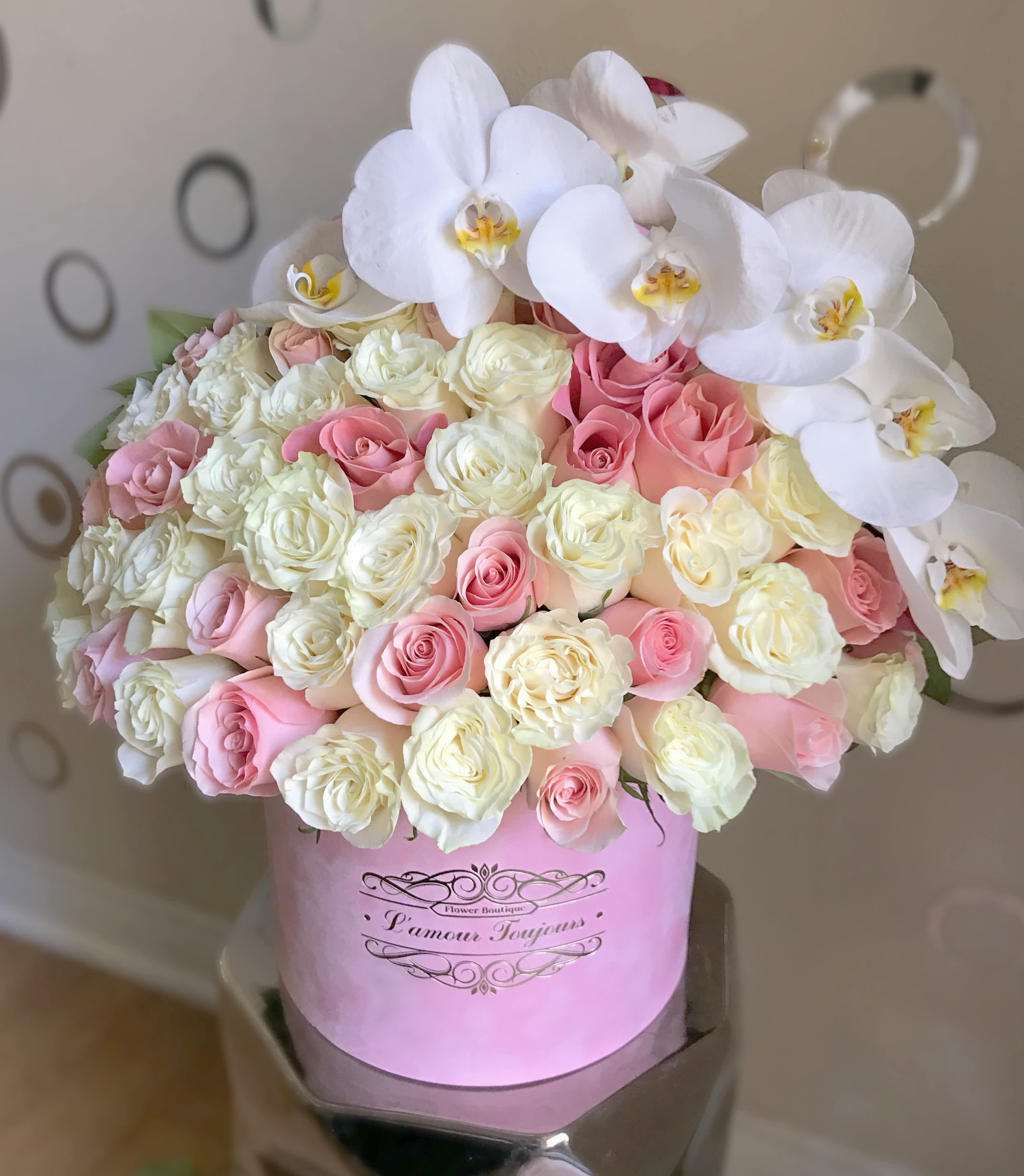 Pink and white roses with white orchids in a pink hat box