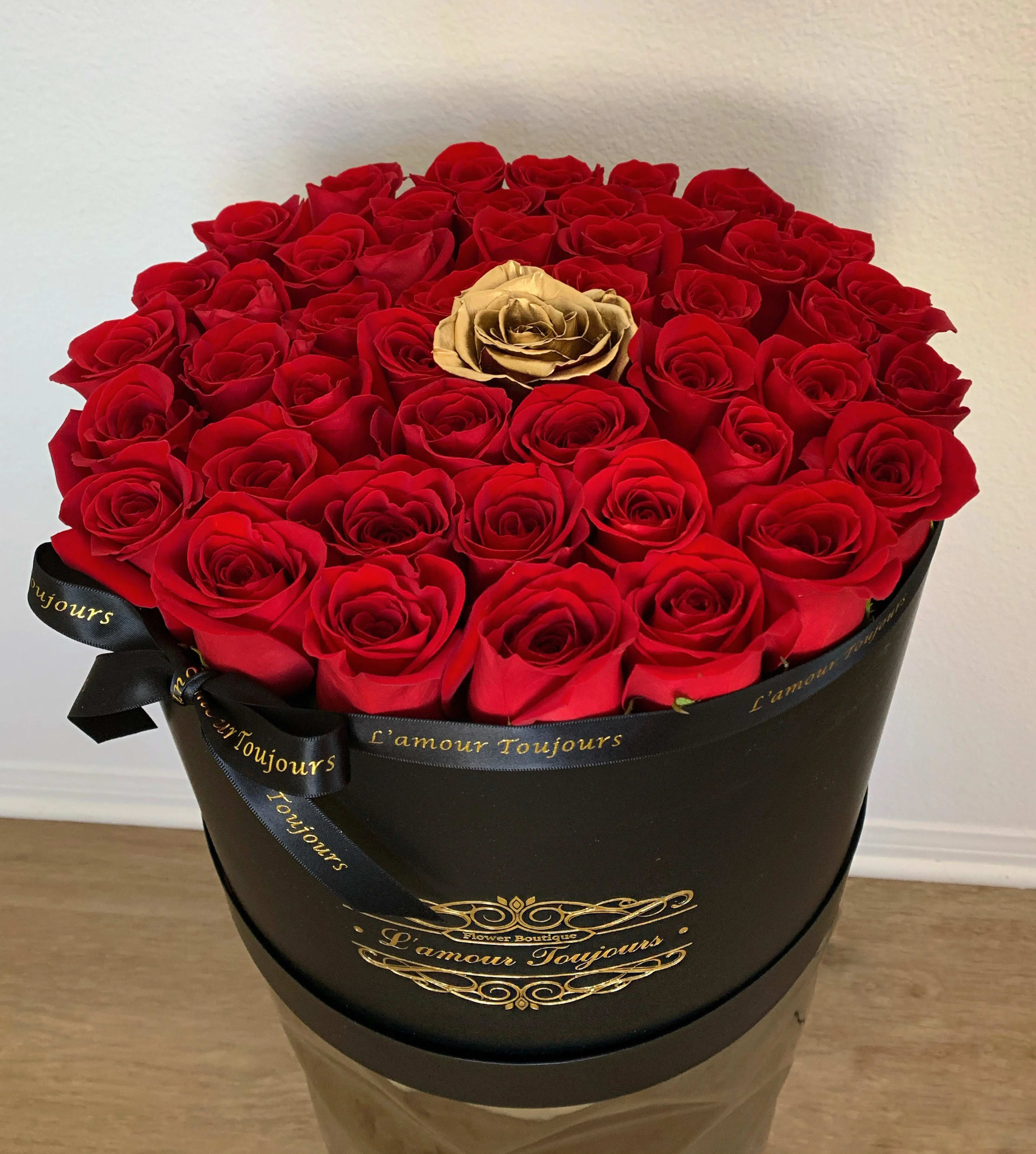 Red roses in a black round box with a gold rose at center