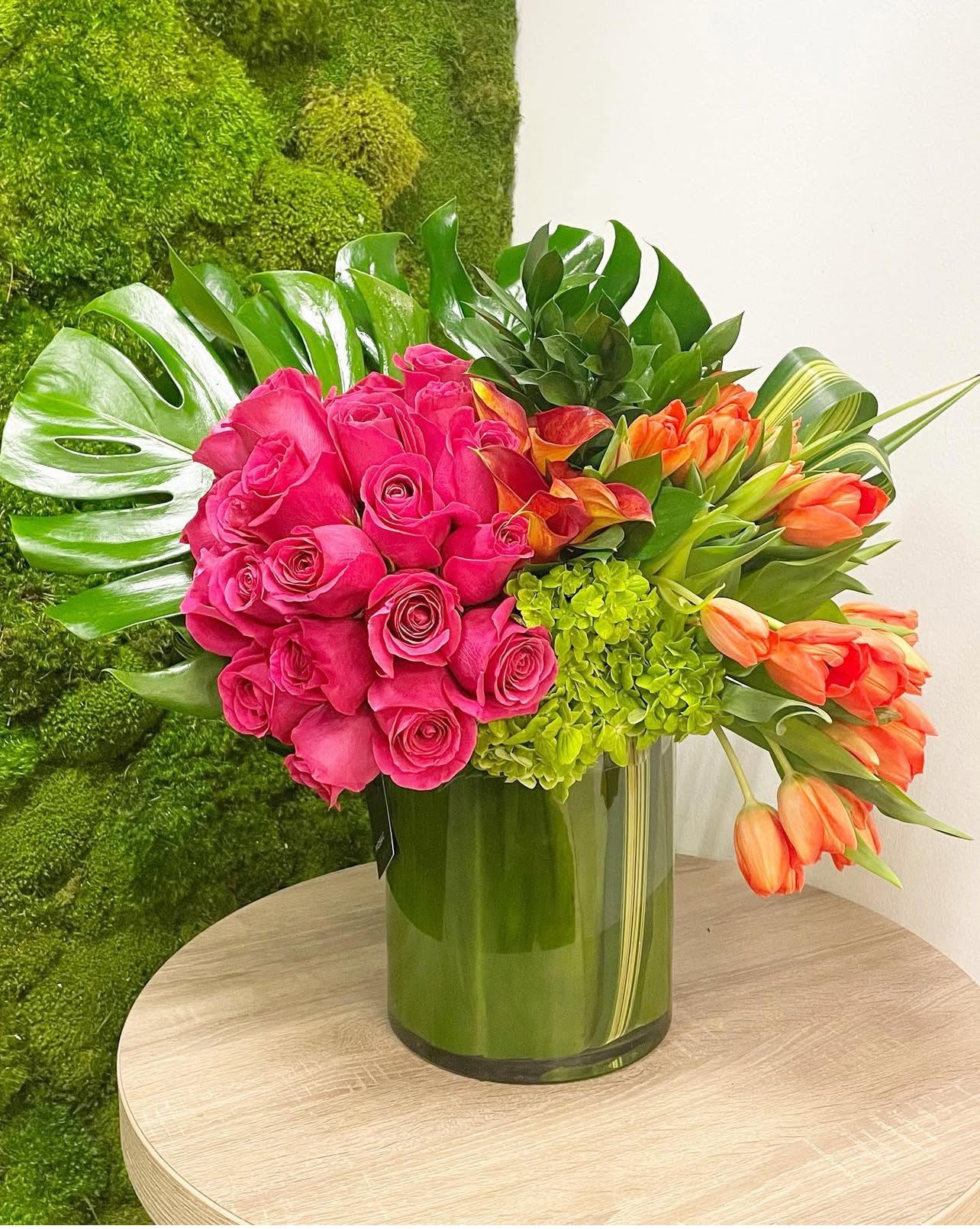 Tropical Sunset - "Tropical Sunset" captures the vibrant energy of a tropical sunset.  The warm orange hues of the tulips and calla lilies are beautifully complemented by the soft pink roses, creating a lively and unforgettable display.  Lush monstera leaves and green hydrangeas add a touch of exotic flair, transporting you to a lush paradise.