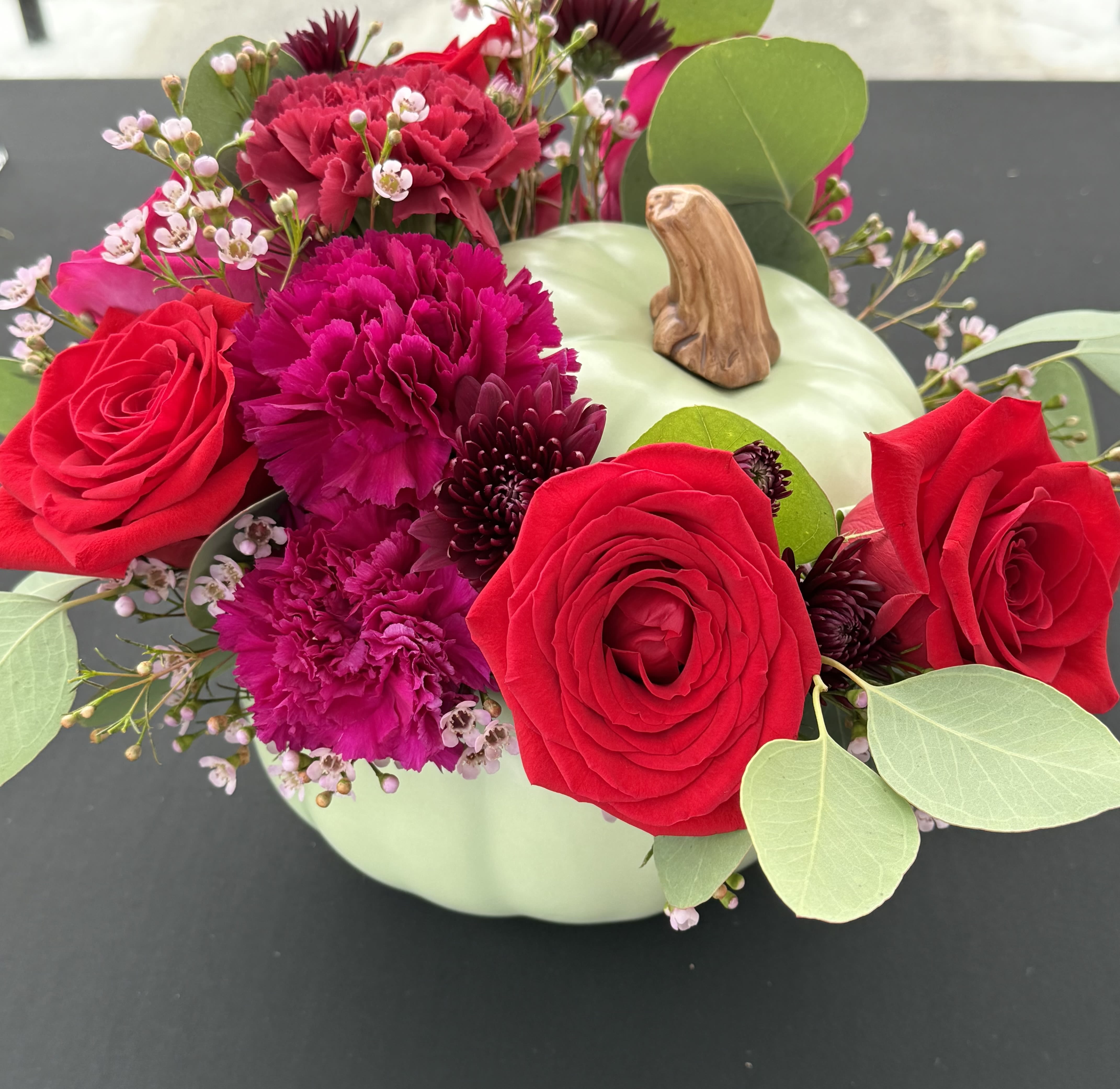 Red roses and magenta carnations arranged in a pale green pumpkin vase