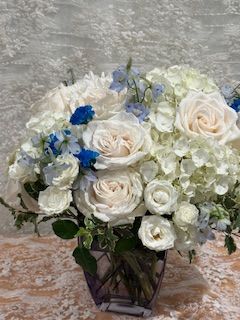 Cherished - Sympathy arrangement filled with white Hydrangea, Roses, Mini roses, Mums and blue delphinium.     If a particular flower, is unavailable, an item of similar quality and value will be substituted.