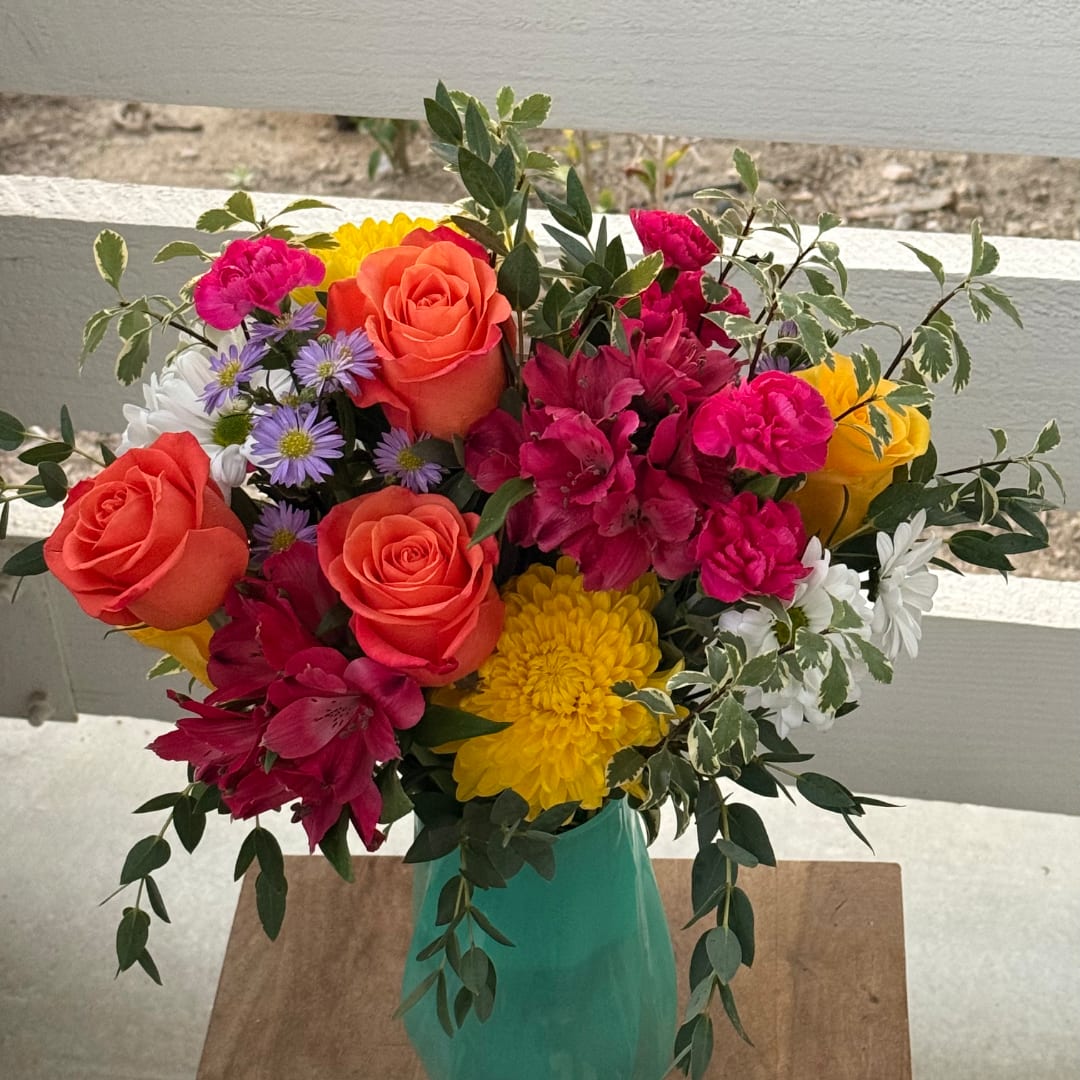 Colorful mixed bouquet in a turquoise vase with roses, daisies, and carnations