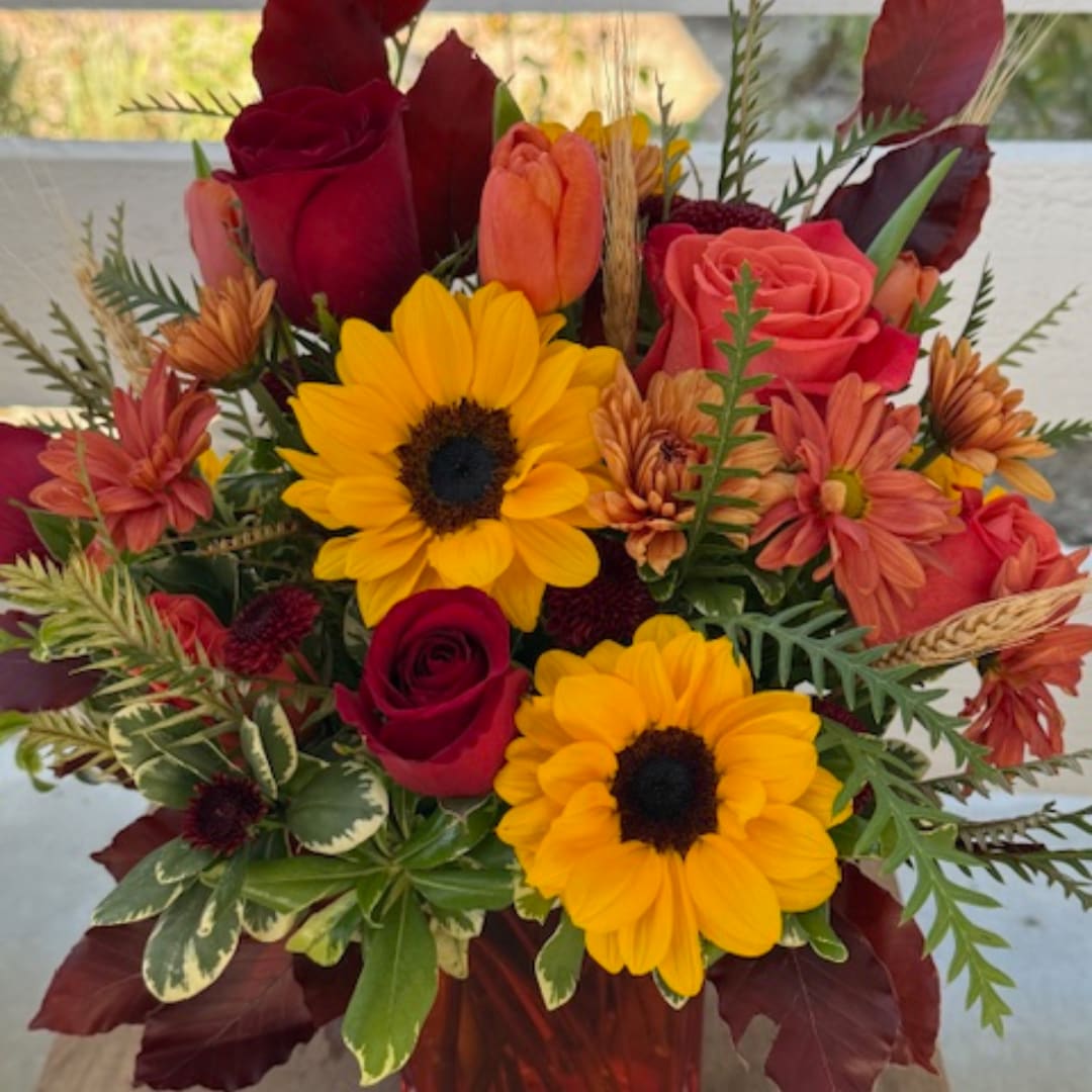 Bouquet of red roses and yellow sunflowers with orange blooms in a vase
