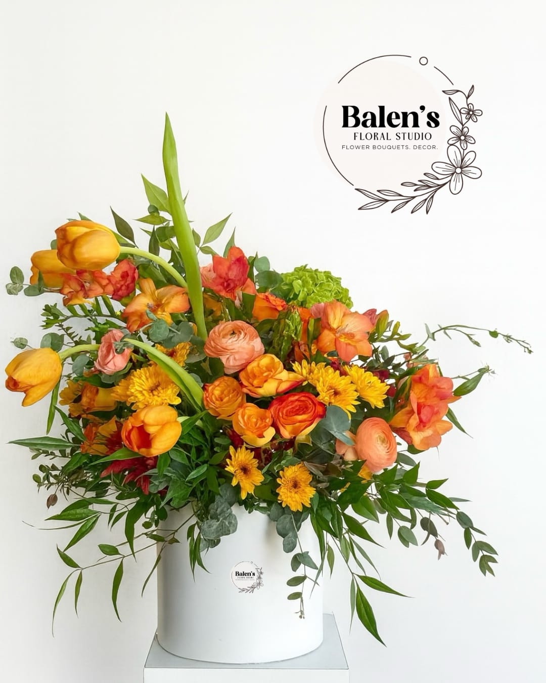 Orange and yellow mixed flower arrangement in a white hatbox