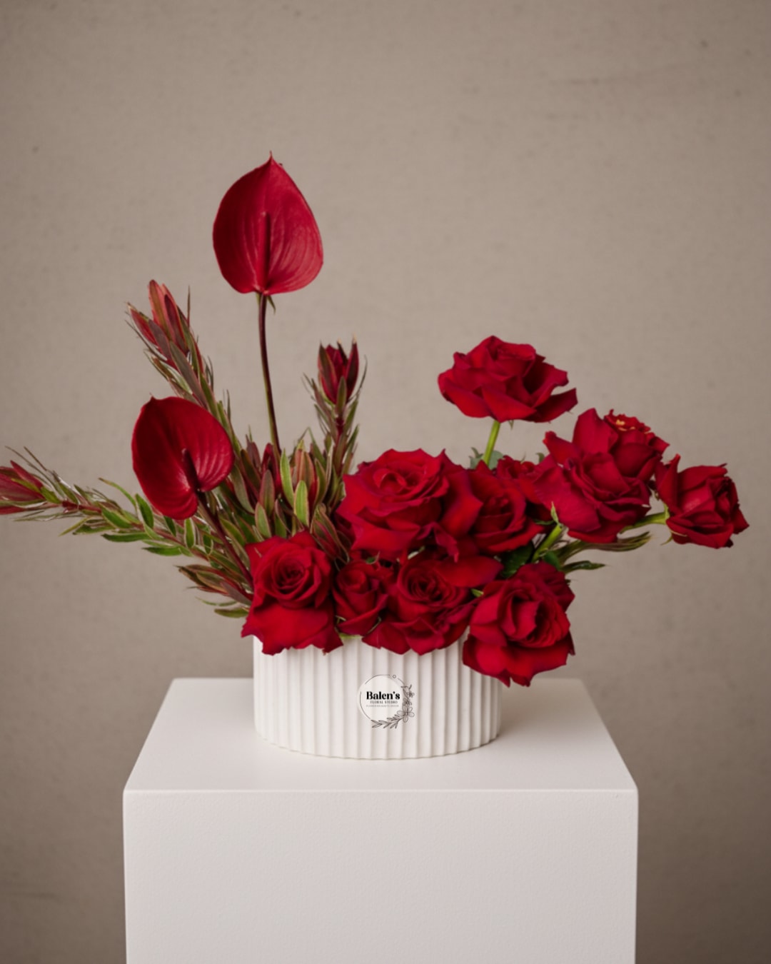 Red roses and burgundy tropical blooms in a white ribbed vase