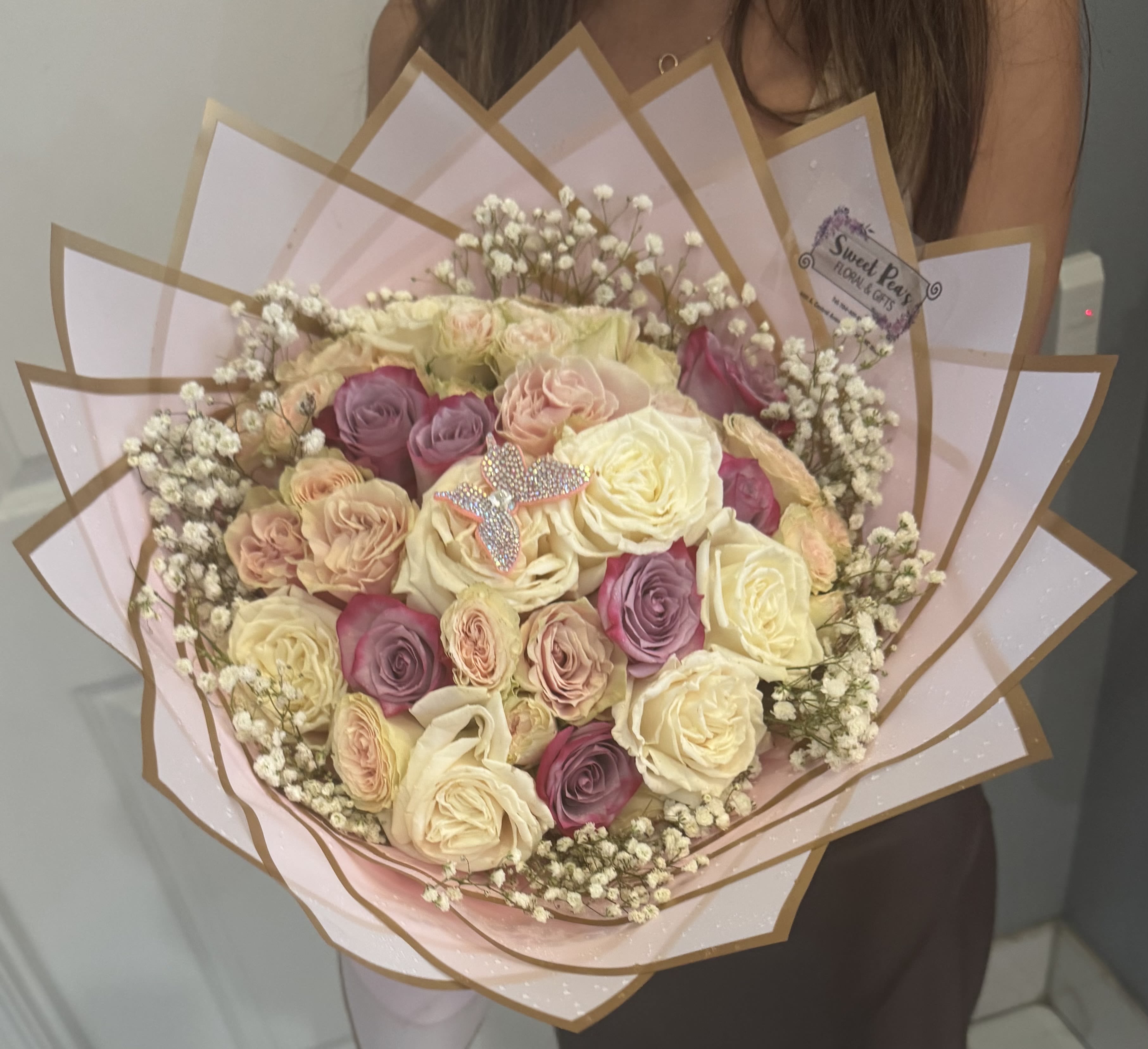 Handheld bouquet of cream, pink, and lavender roses wrapped in pink paper