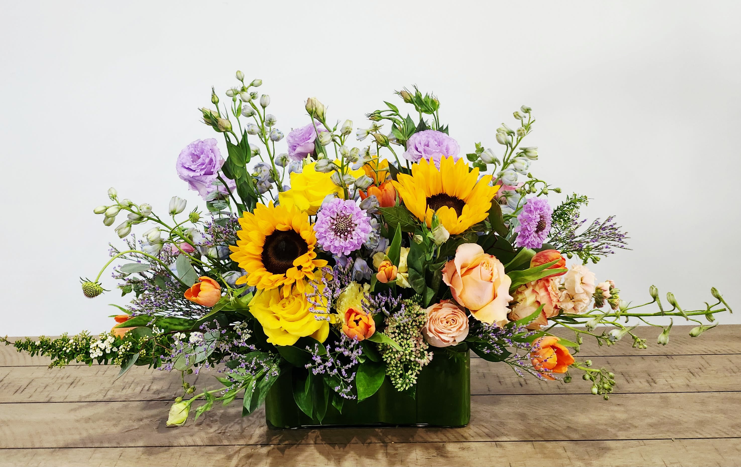 Mixed bouquet with sunflowers, roses, and purple blooms in a green vase