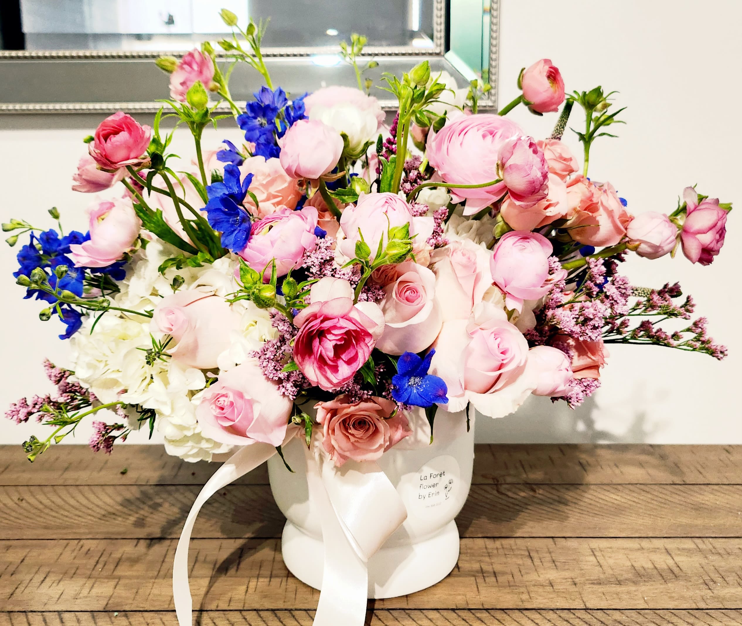 Pink and blue mixed flower arrangement in a white vase with ribbon