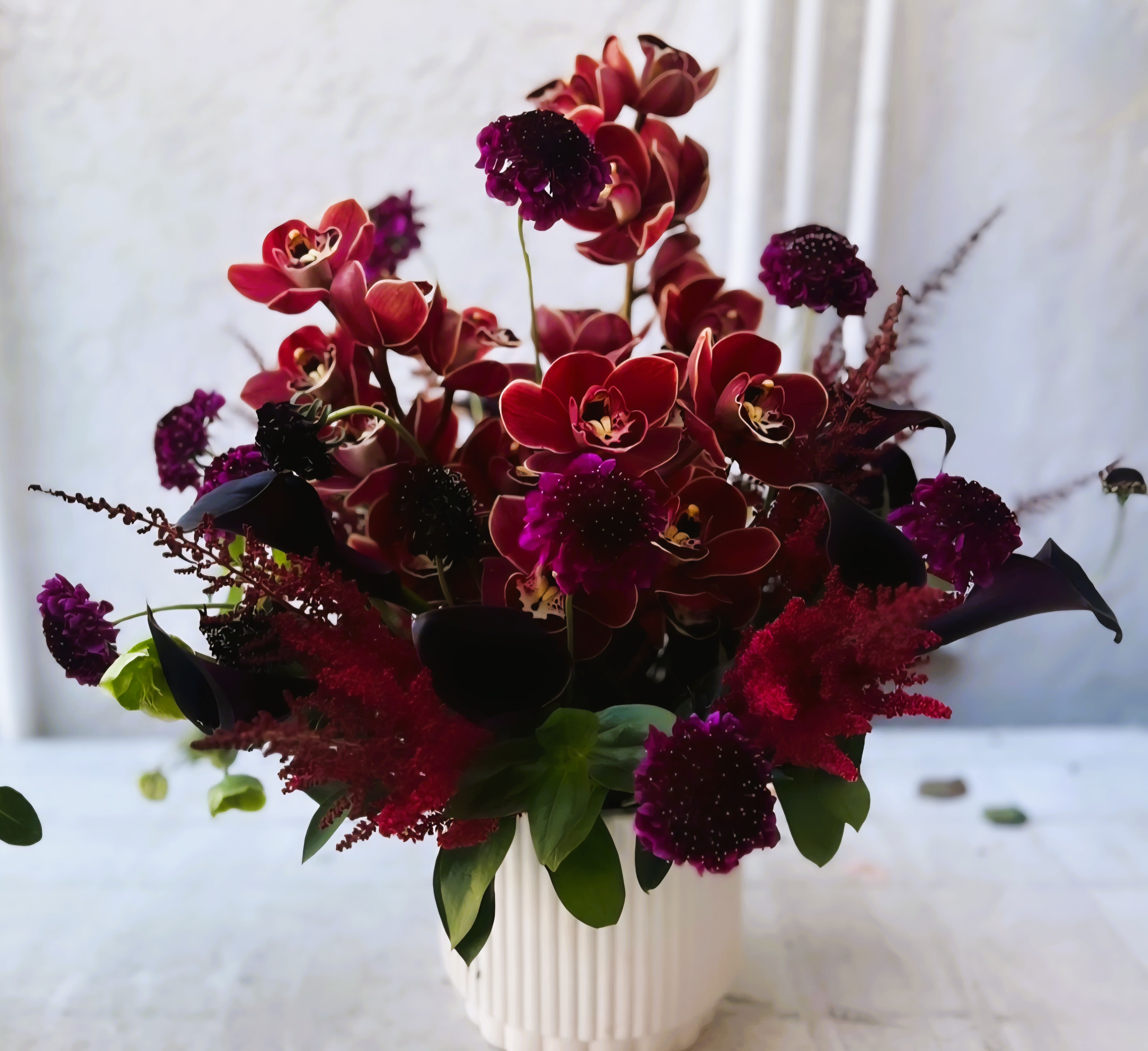 Deep red orchid arrangement in a white vase with dark purple accents