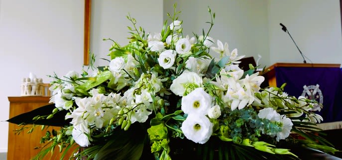 Large white lily and lisianthus spray with green accents displayed in a church setting