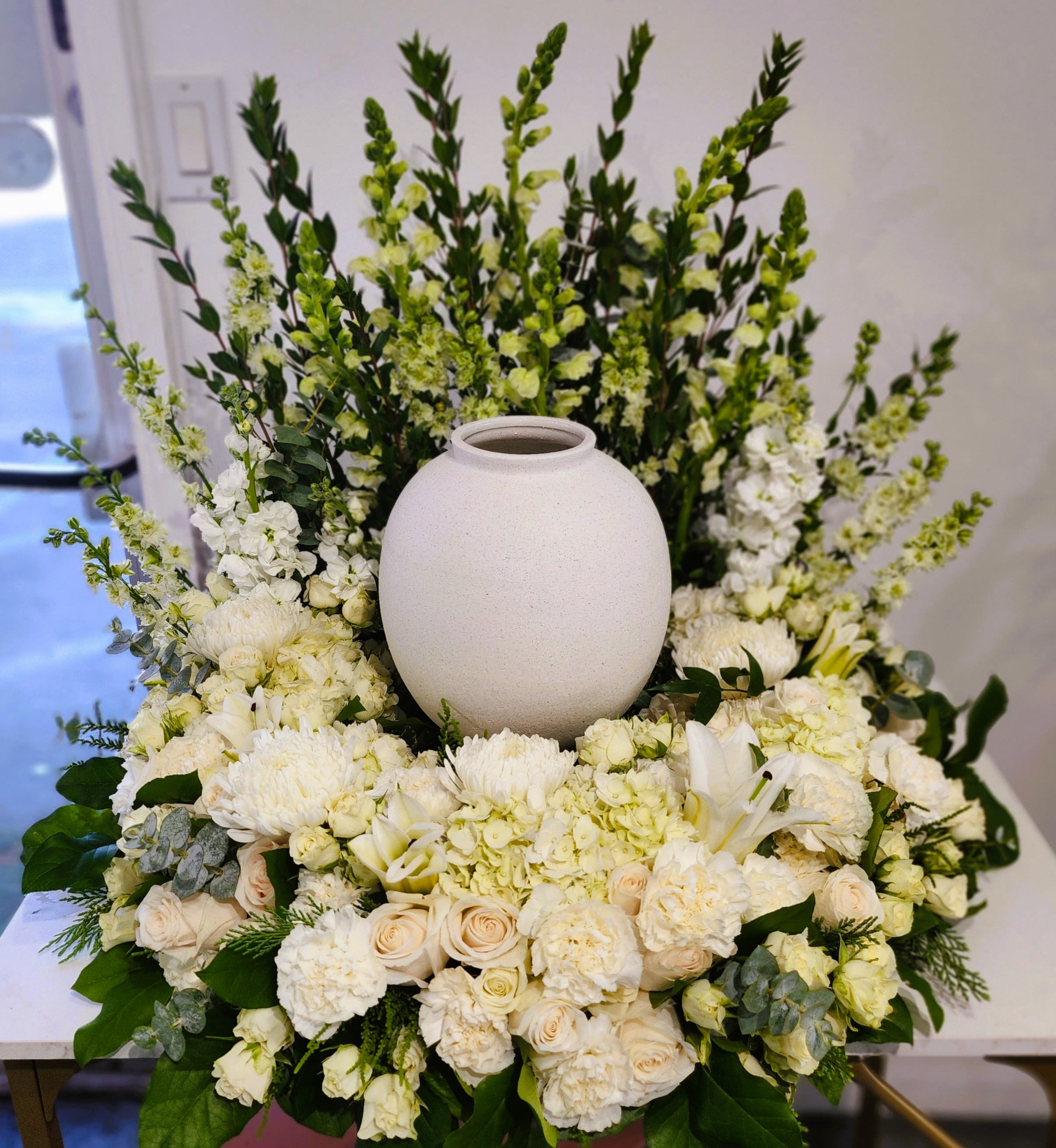 White floral arrangement surrounding a round white urn