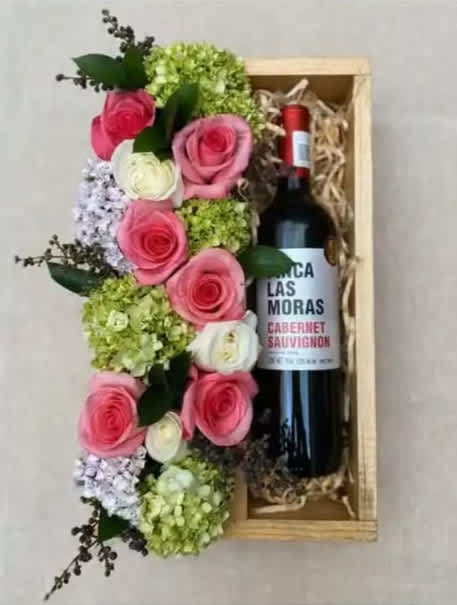 Pink and white roses arranged beside a wine bottle in a wooden gift box