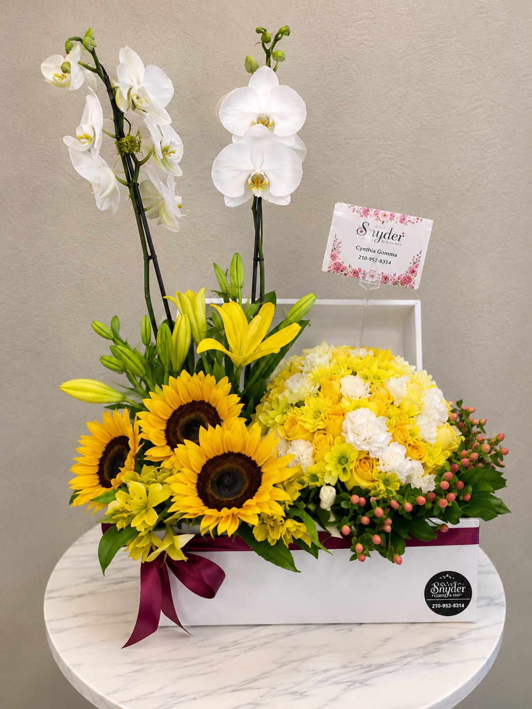 Yellow and white floral arrangement with orchids, sunflowers, and roses in a white box