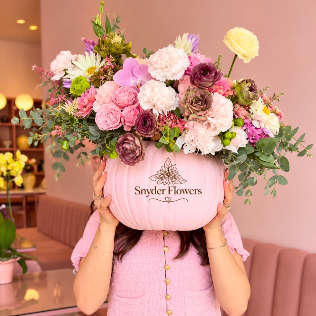 Pink pumpkin container filled with mixed flowers and greenery