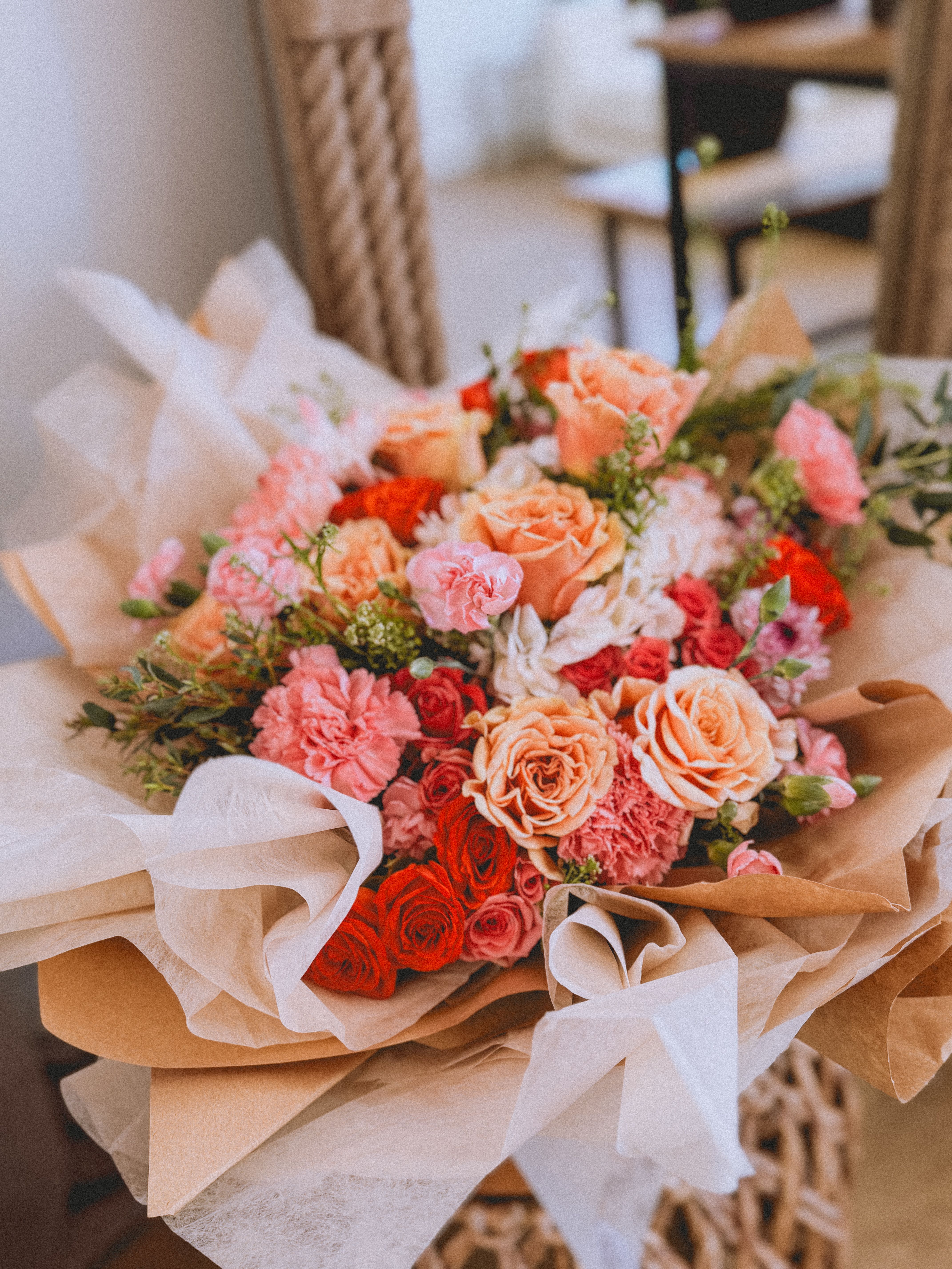 Bouquet of peach, pink, and red roses with carnations wrapped in brown paper