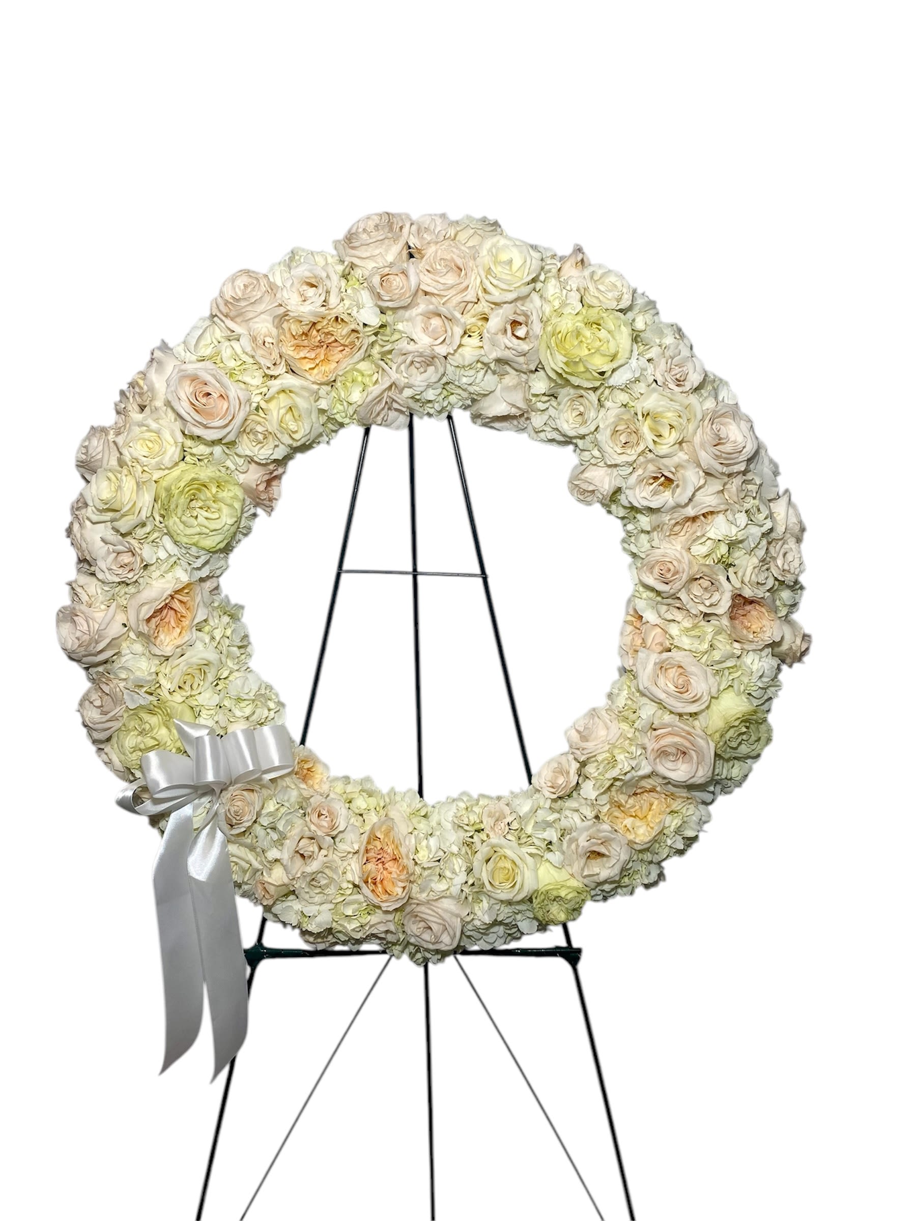 Cream floral wreath on a black stand with a silver ribbon