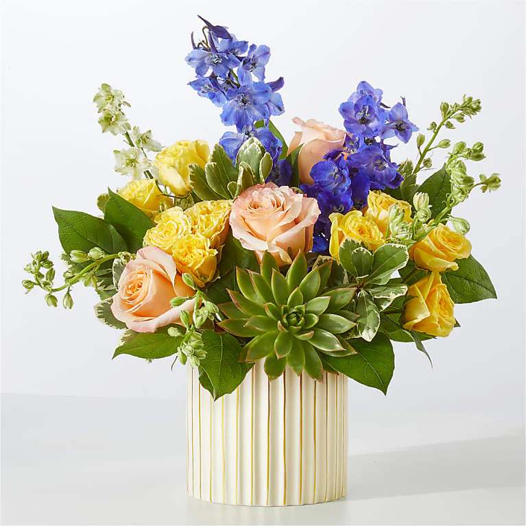 Bouquet of peach and yellow roses with blue flowers in a striped vase