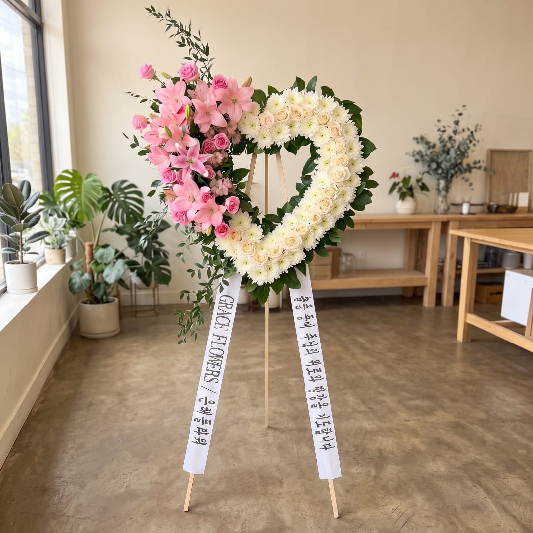 Heart-shaped floral wreath on a stand with pink and white flowers