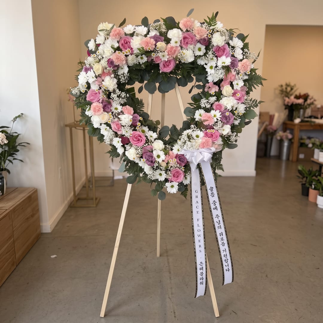 Heart-shaped floral wreath on a stand with pink, white, and purple flowers