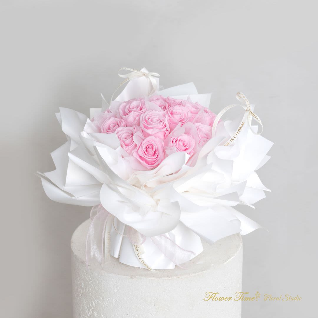 Pink rose bouquet wrapped in white paper on a white pedestal