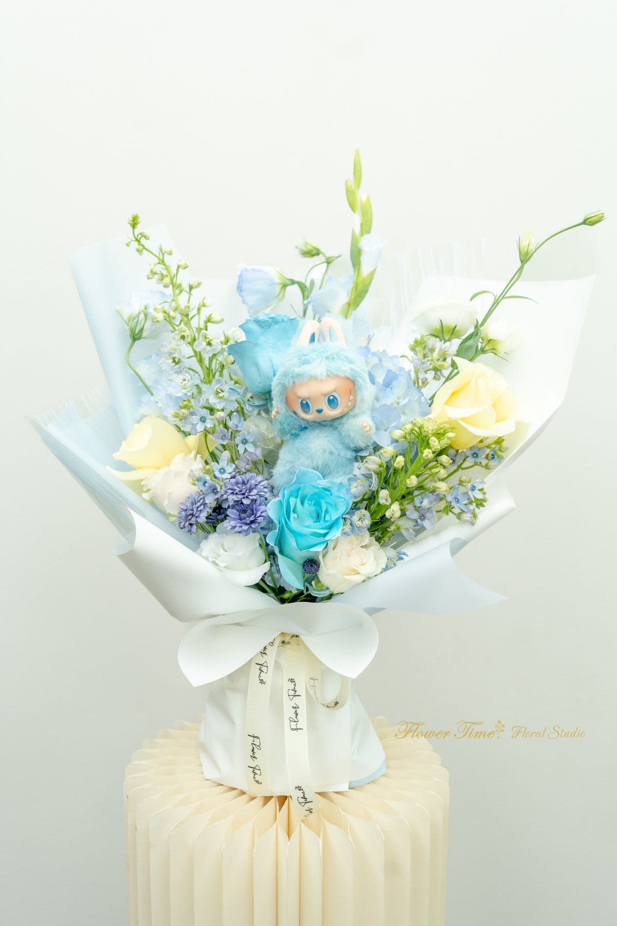 Blue plush toy in a bouquet of pastel flowers with white wrapping