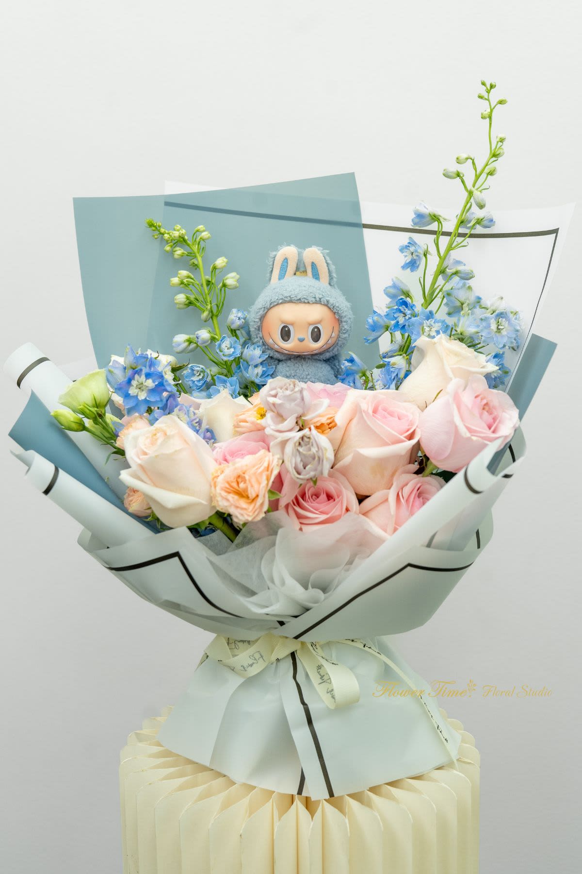 Bouquet of pink and white roses with blue flowers and a plush character centerpiece