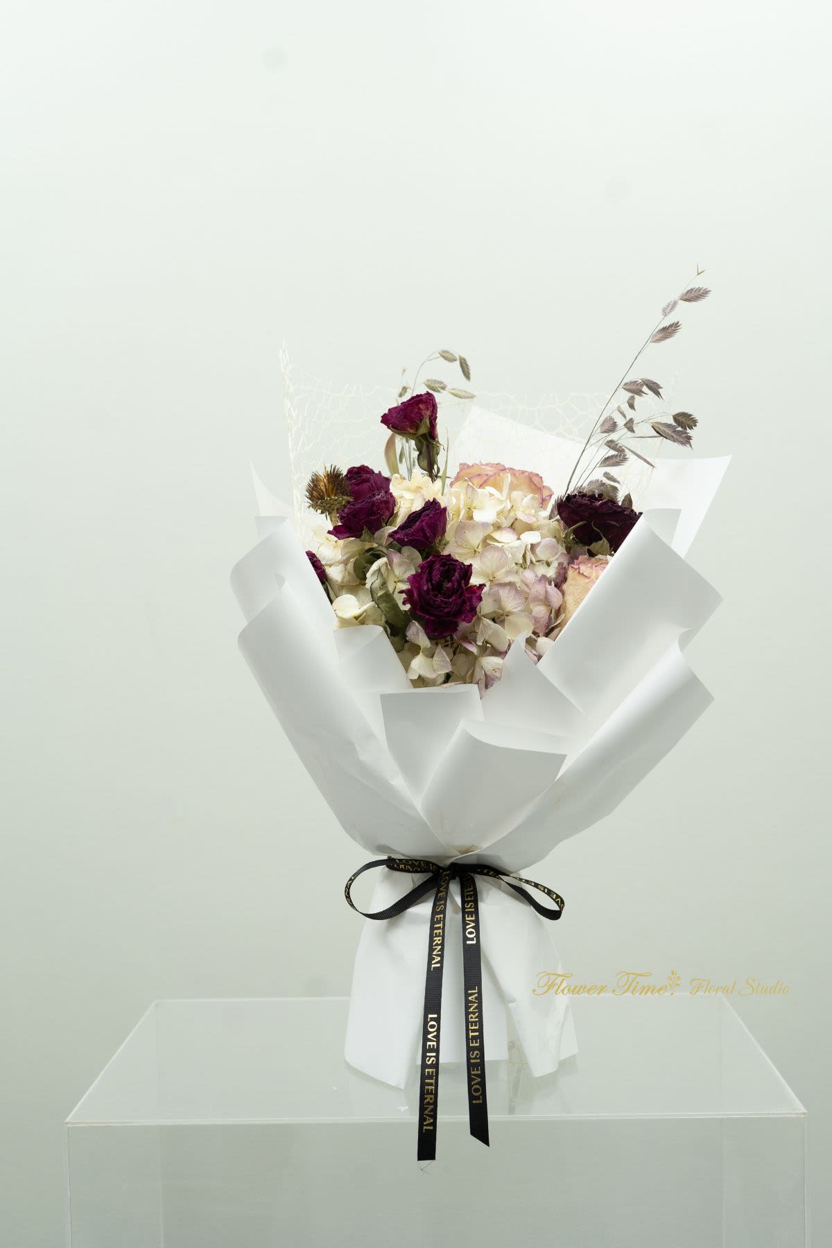 Bouquet of dark purple roses and pale hydrangeas wrapped in white paper