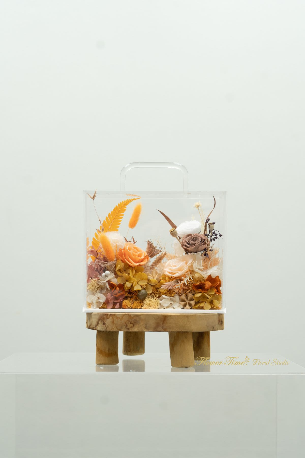 Clear box arrangement with orange and cream roses on a wooden stand