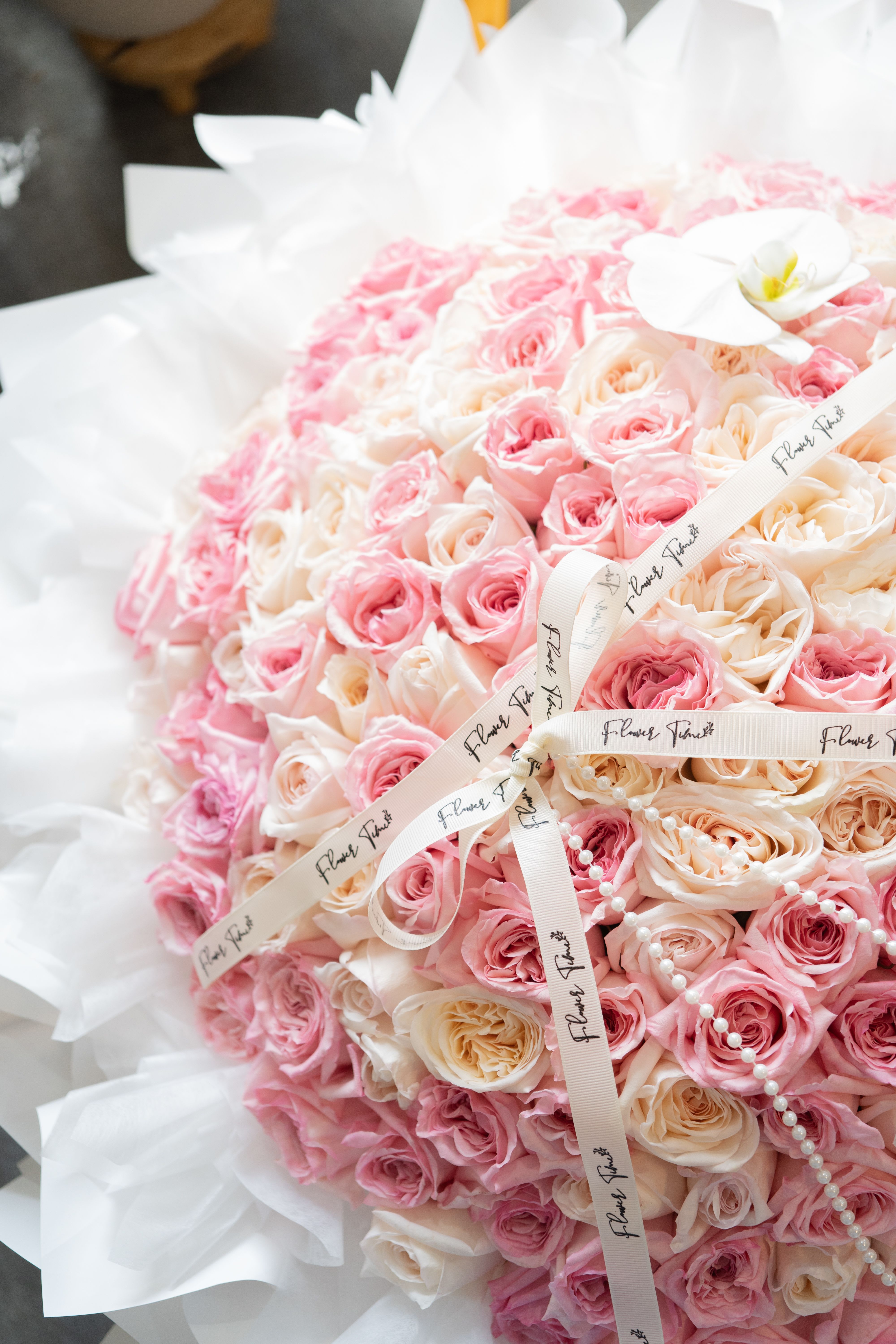 Large bouquet of pink and cream roses wrapped in white paper with ribbon