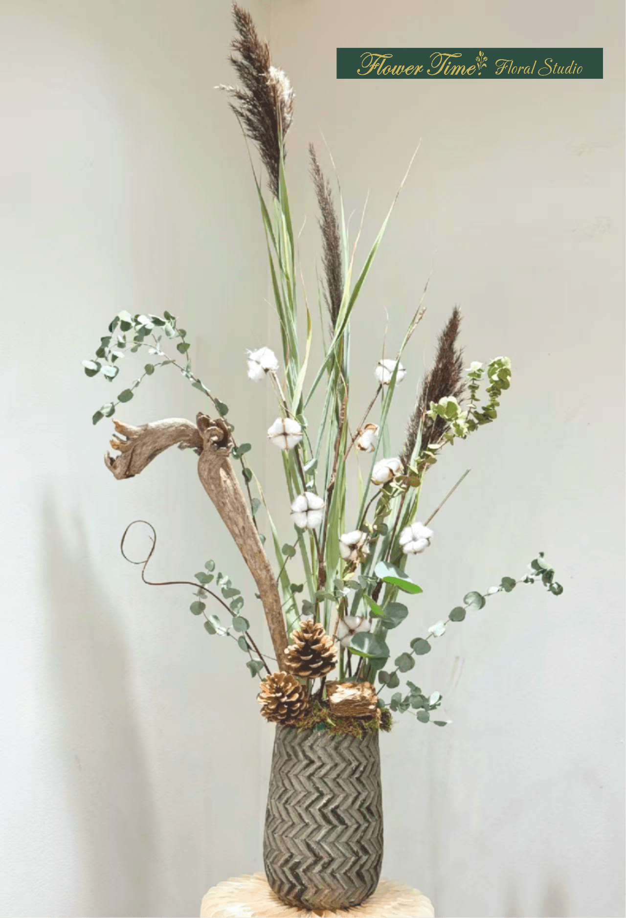 Tall dried floral arrangement in a patterned vase with cotton and pinecones