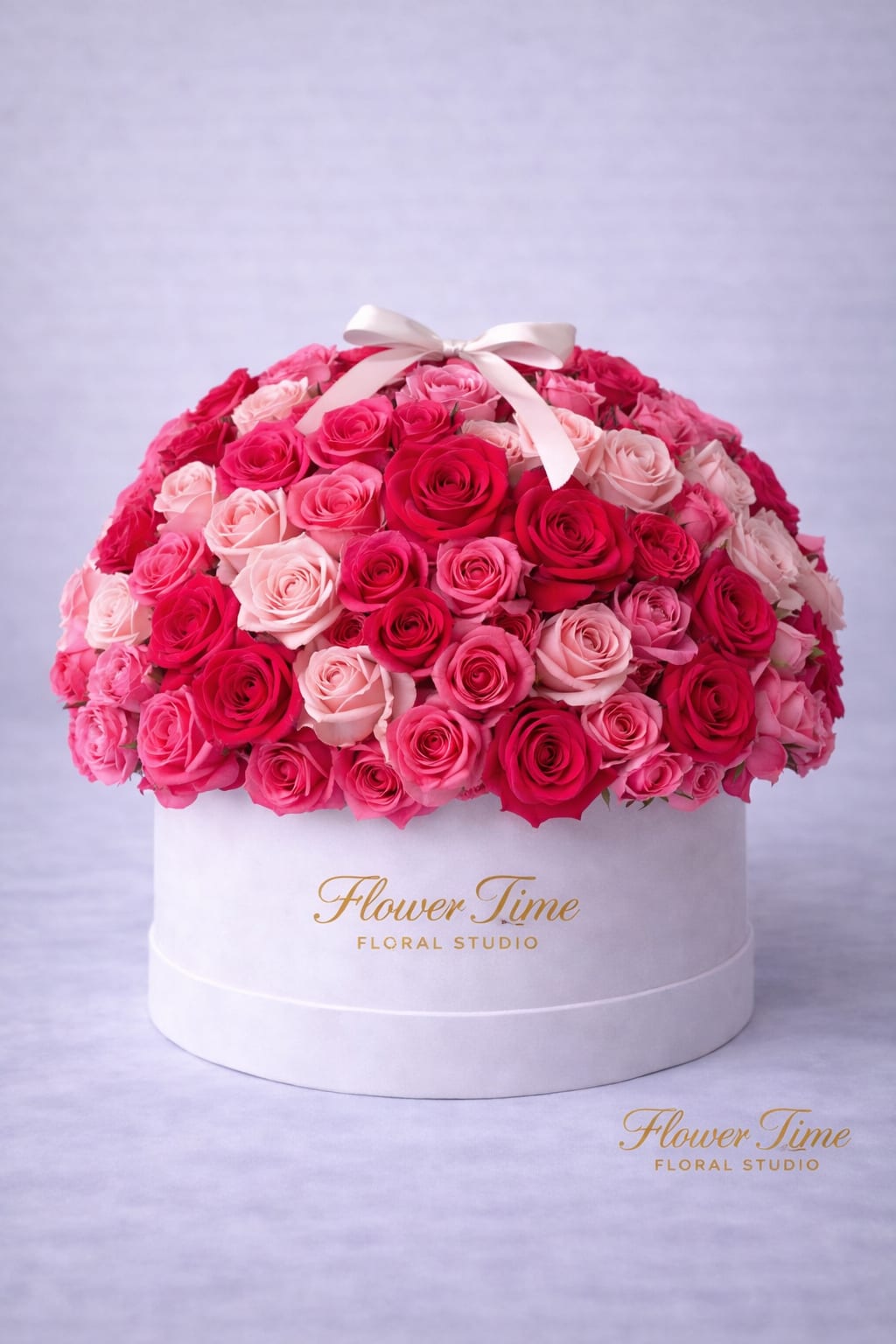 Round box arrangement of pink and red roses with a white ribbon bow