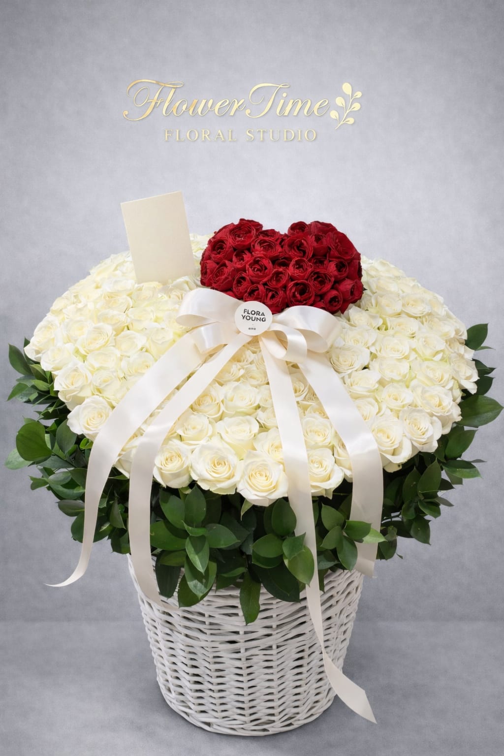 Heart-shaped red and white rose arrangement in a white basket with ribbon