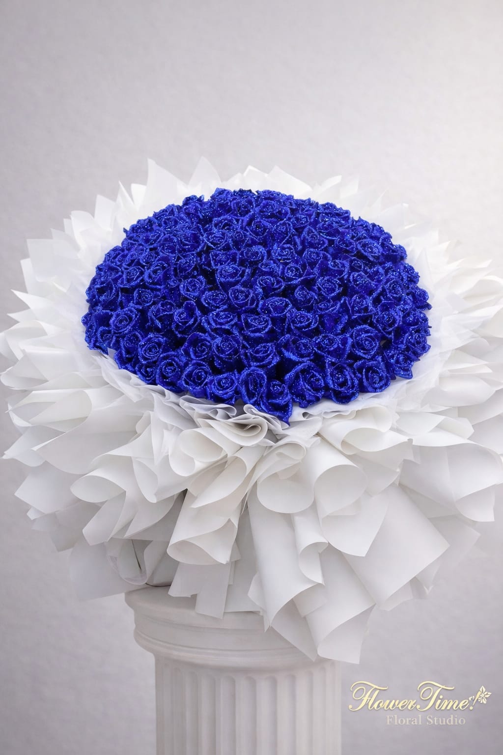 Blue rose bouquet with white wrapping in a pedestal vase