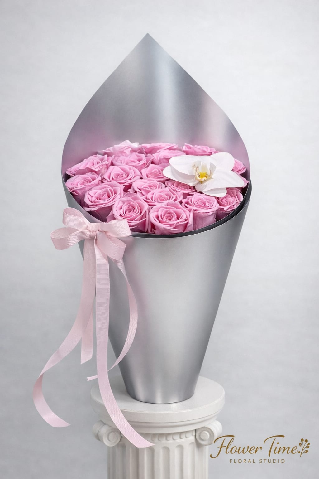 Pink roses in a silver cone wrap with a white orchid accent and pink ribbon