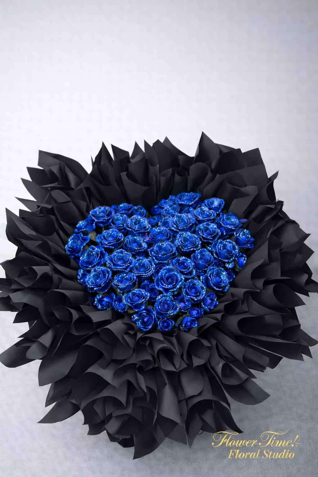 Heart-shaped bouquet of blue roses wrapped in black paper