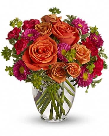 Orange roses and magenta daisies in a clear glass vase