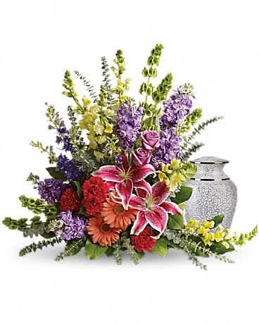 Mixed floral arrangement with lilies, roses, and gerbera daisies beside a silver urn