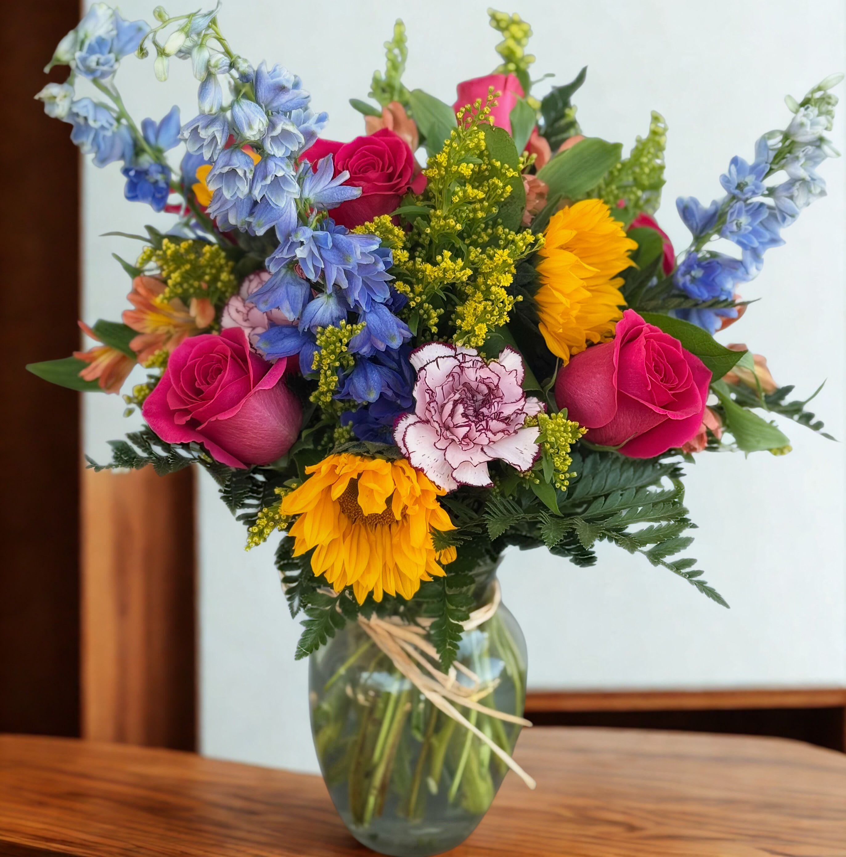 Mixed bouquet of roses, sunflowers, and blue flowers in a glass vase