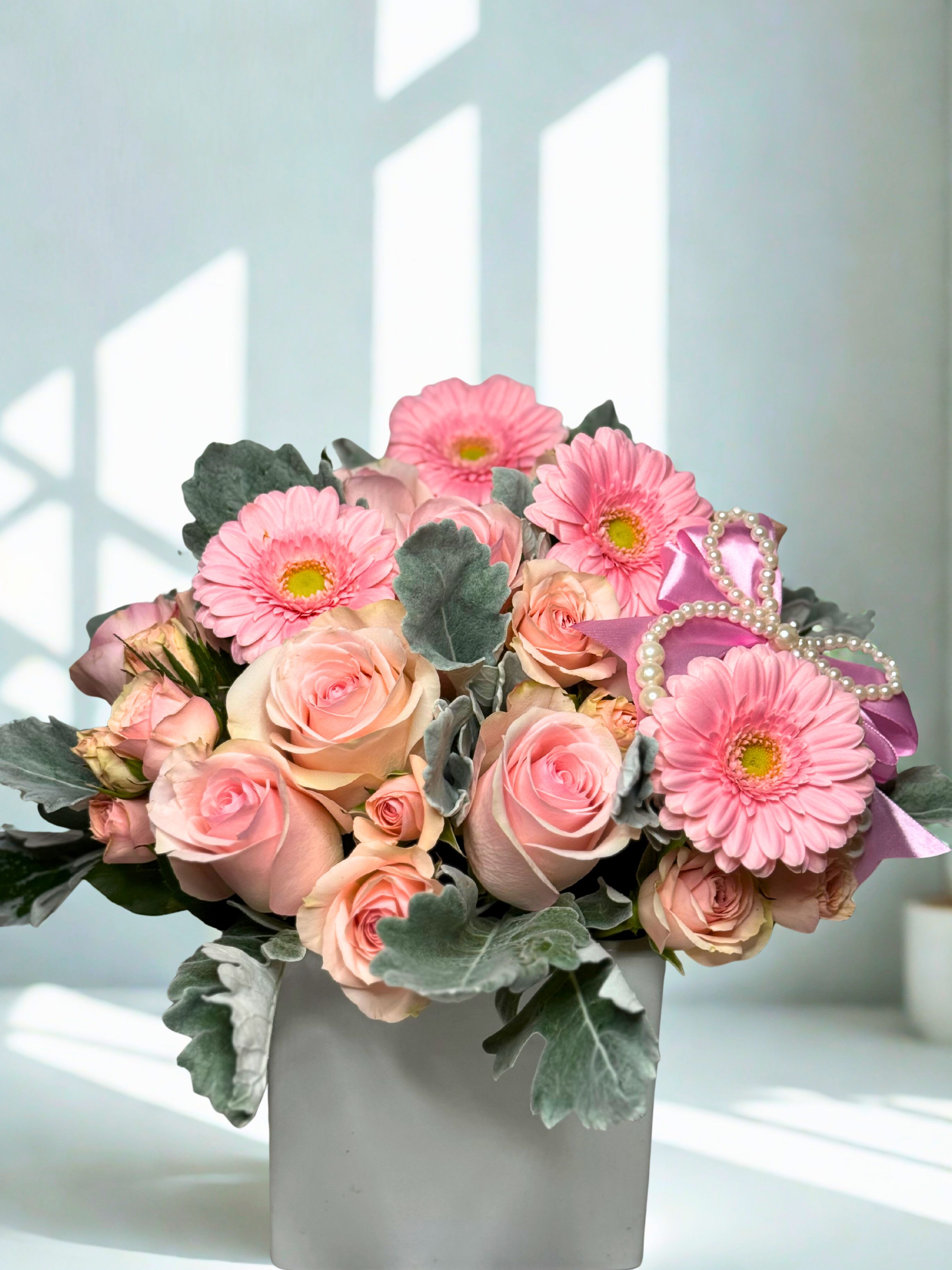 Pink roses and gerbera daisies in a white vase with a ribbon bow